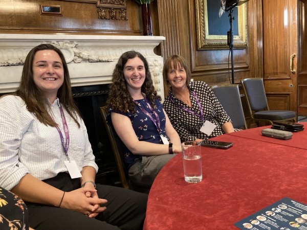 Three women sat at a table, looking and smiling at the camera