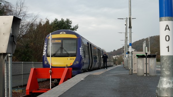 Image of a stationary train at a platform in Tweedback station with a ticket guard walking