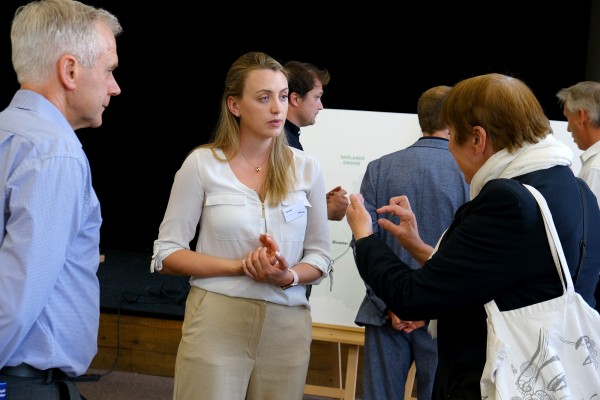 Two members of the public facing away from the camera, talking to an EWR colleague at an event inside a village hall